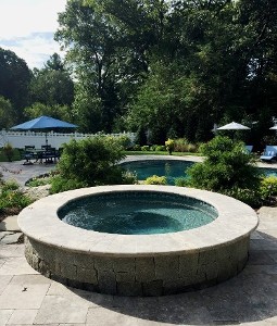 Travertine topped hot tub overlooking pool and lush landscape by New View